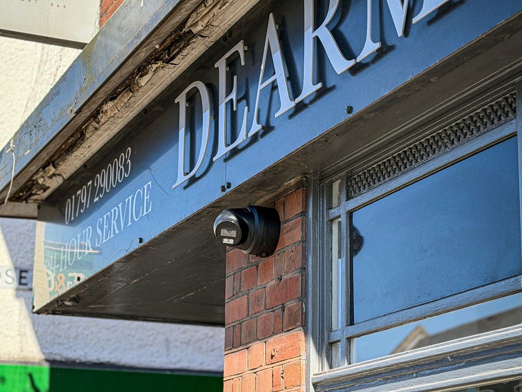 Black turret camera under the Dearman Bartlett funeral directors sign on New Romney High Street